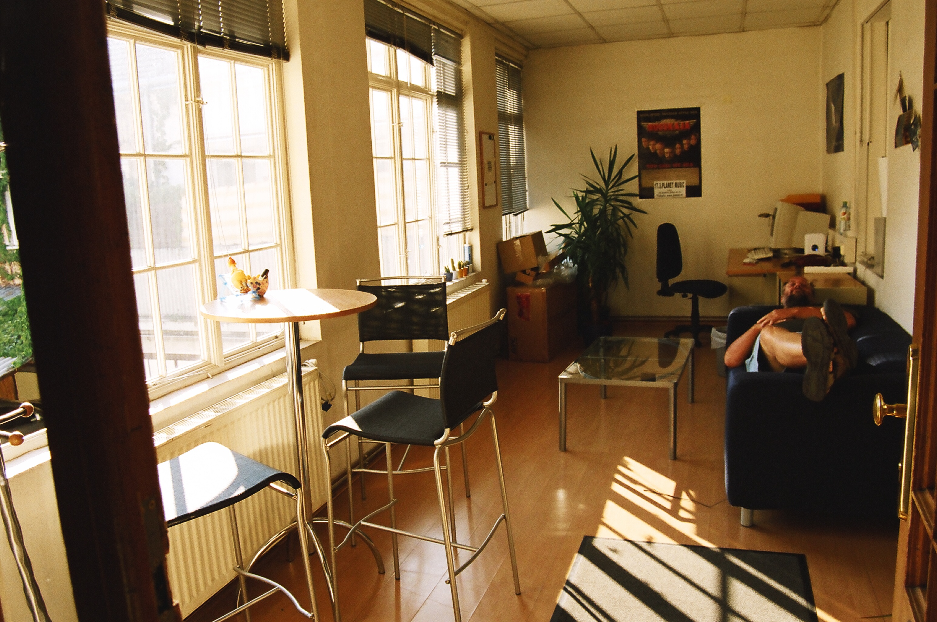 Sunlit office interior with large windows, a casual seating area, office desk, and a person relaxing on a blue sofa.