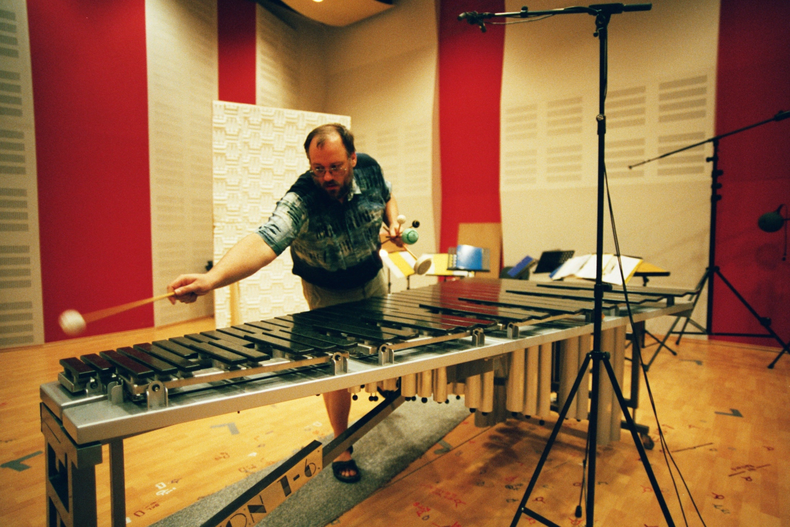 Musician playing a vibraphone or marimba in a recording studio, surrounded by sound-dampening panels and microphones.