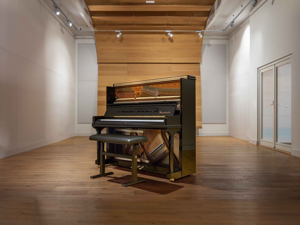 Bösendorfer Grand Upright 130 piano with open top and bench, showcasing its strings and hammers, in a modern room with wood floor and ceiling accents.