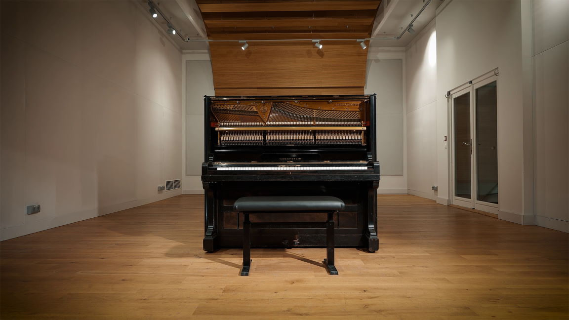 Vintage 1904 C. Bechstein German upright piano in Berlin Kreuzberg, showcasing its exposed inner mechanisms, dark wood finish, and a black bench on a polished wooden floor in a minimalist room with white walls and subtle lighting.