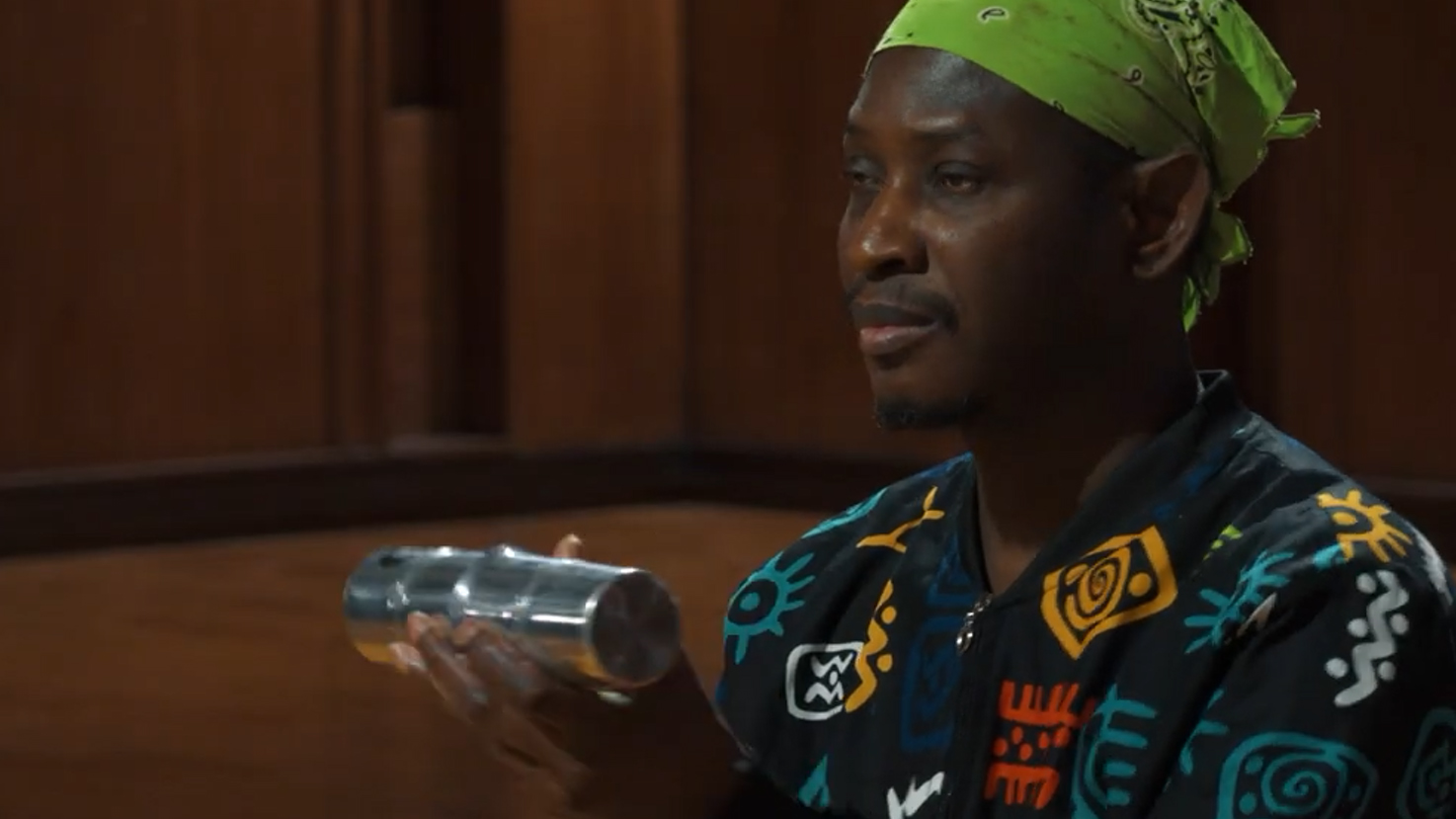 Man in a green bandana and patterned jacket holding a silver shaker.