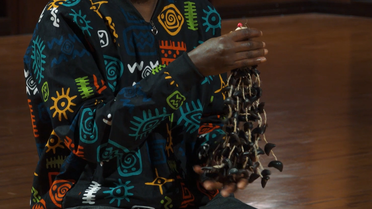 Person in a vibrant patterned shirt holding a traditional African instrument made of shells or seeds on strings.