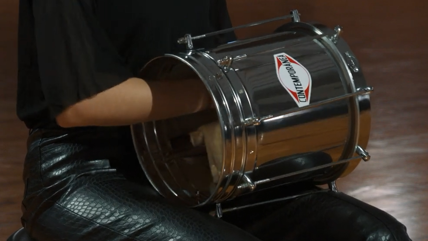 Person wearing black leather pants and shirt playing a chrome Contemporeana drum with their arm inside.