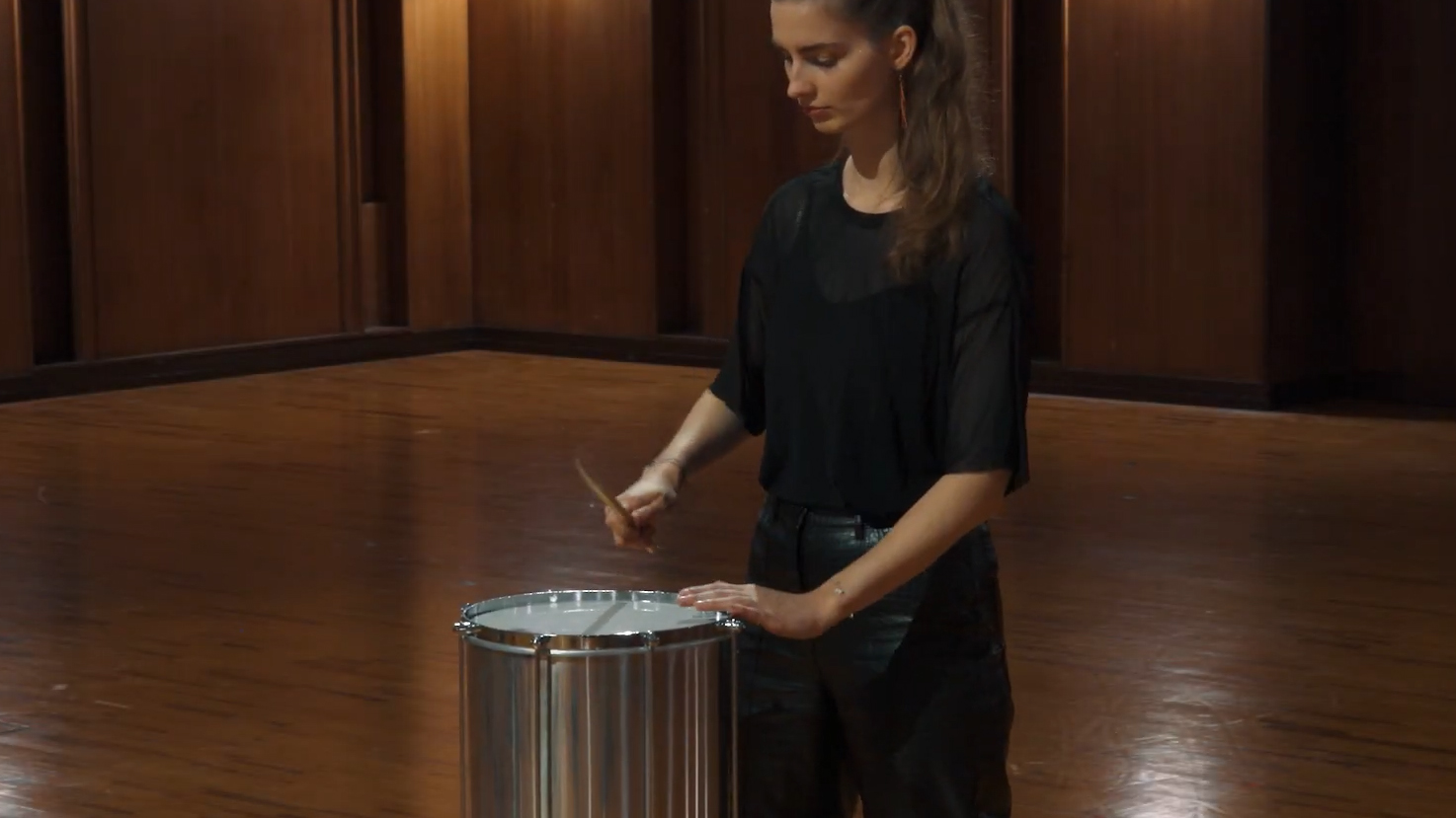 Young woman drumming a pandeiro in a studio with wooden floors.