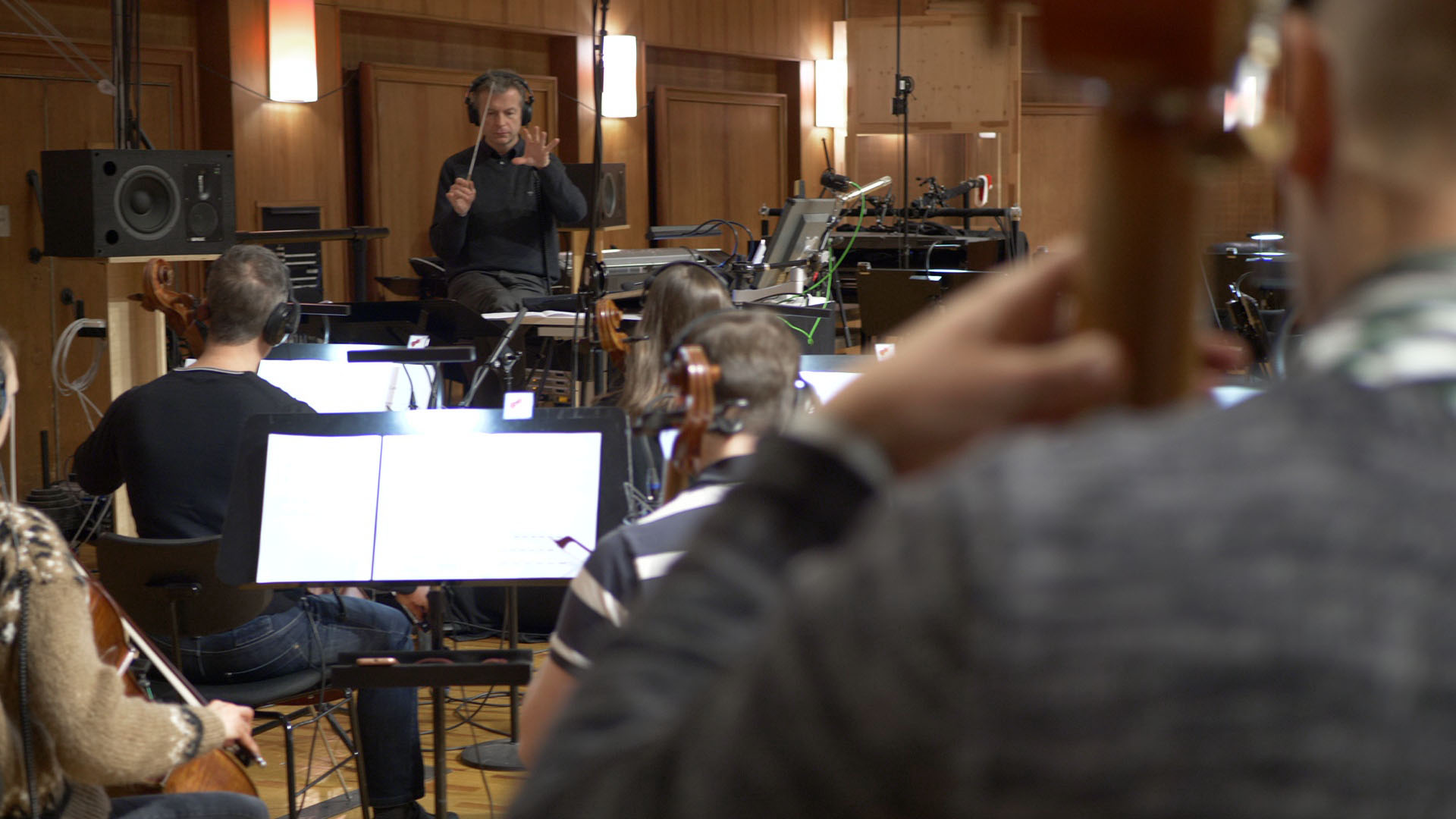 Orchestra conductor with headphones leading musicians with string instruments in a recording studio.