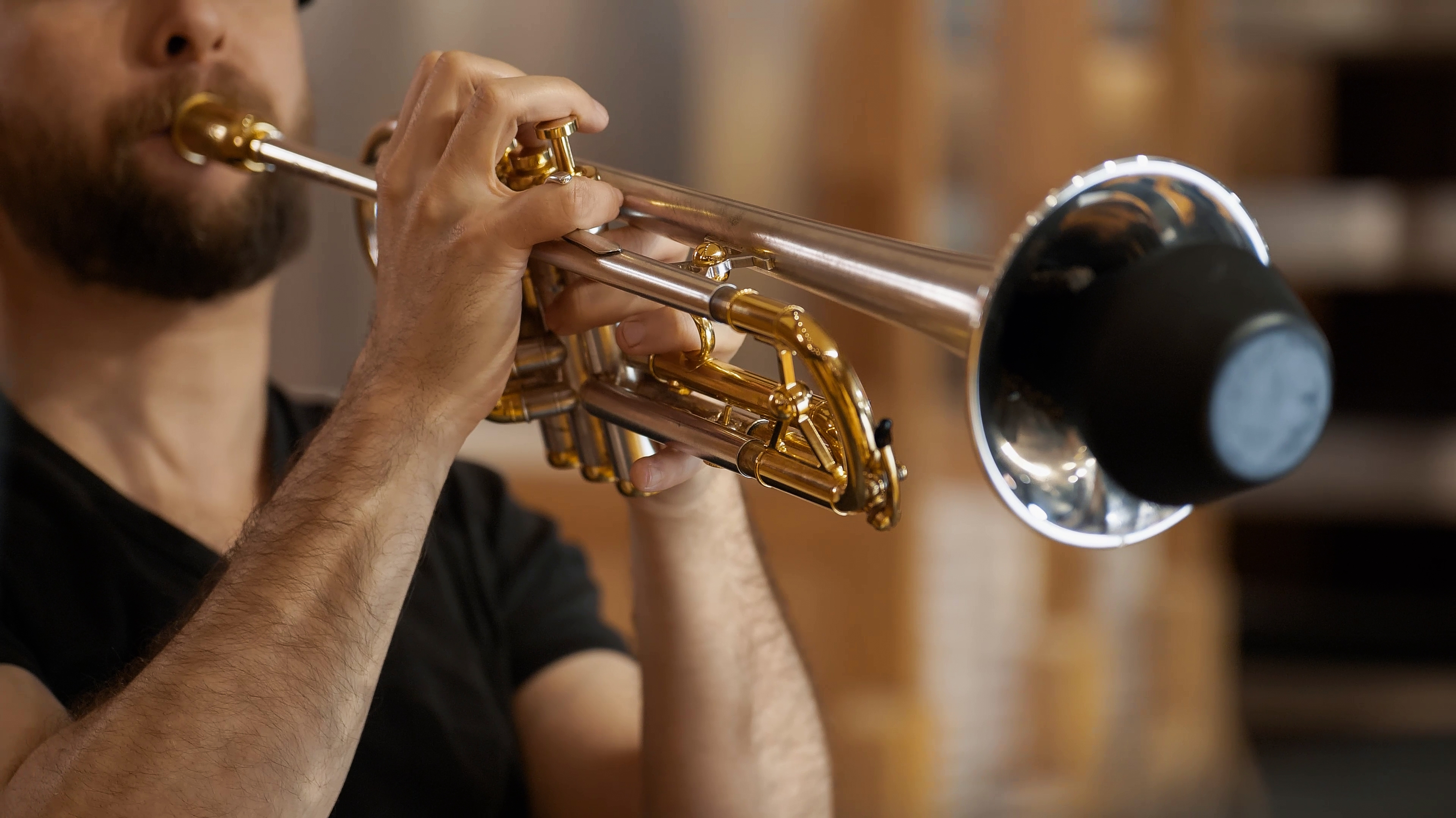 Bearded man in a black shirt playing a silver and gold trumpet with a mute installed, close up from the chest up.