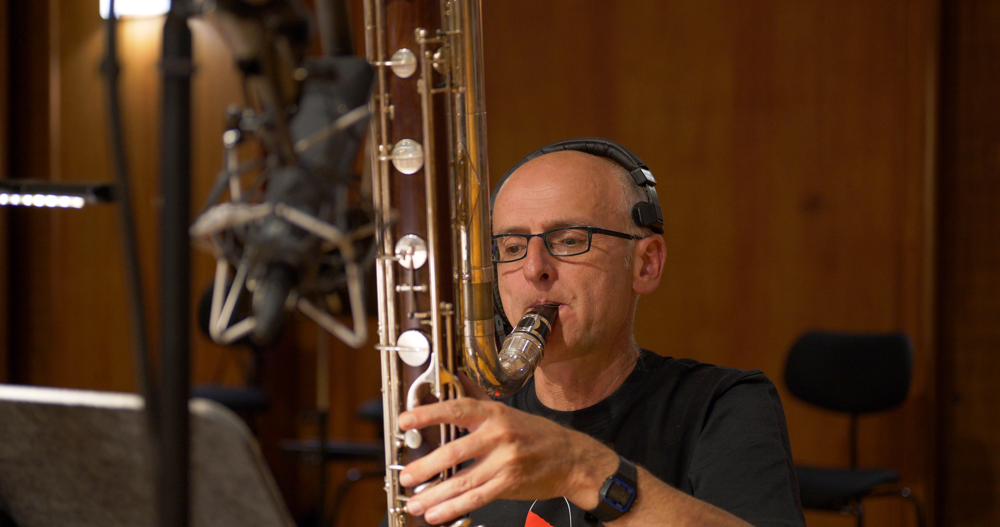 Musician wearing headphones playing a bassoon, recording woodwind instruments in a studio.