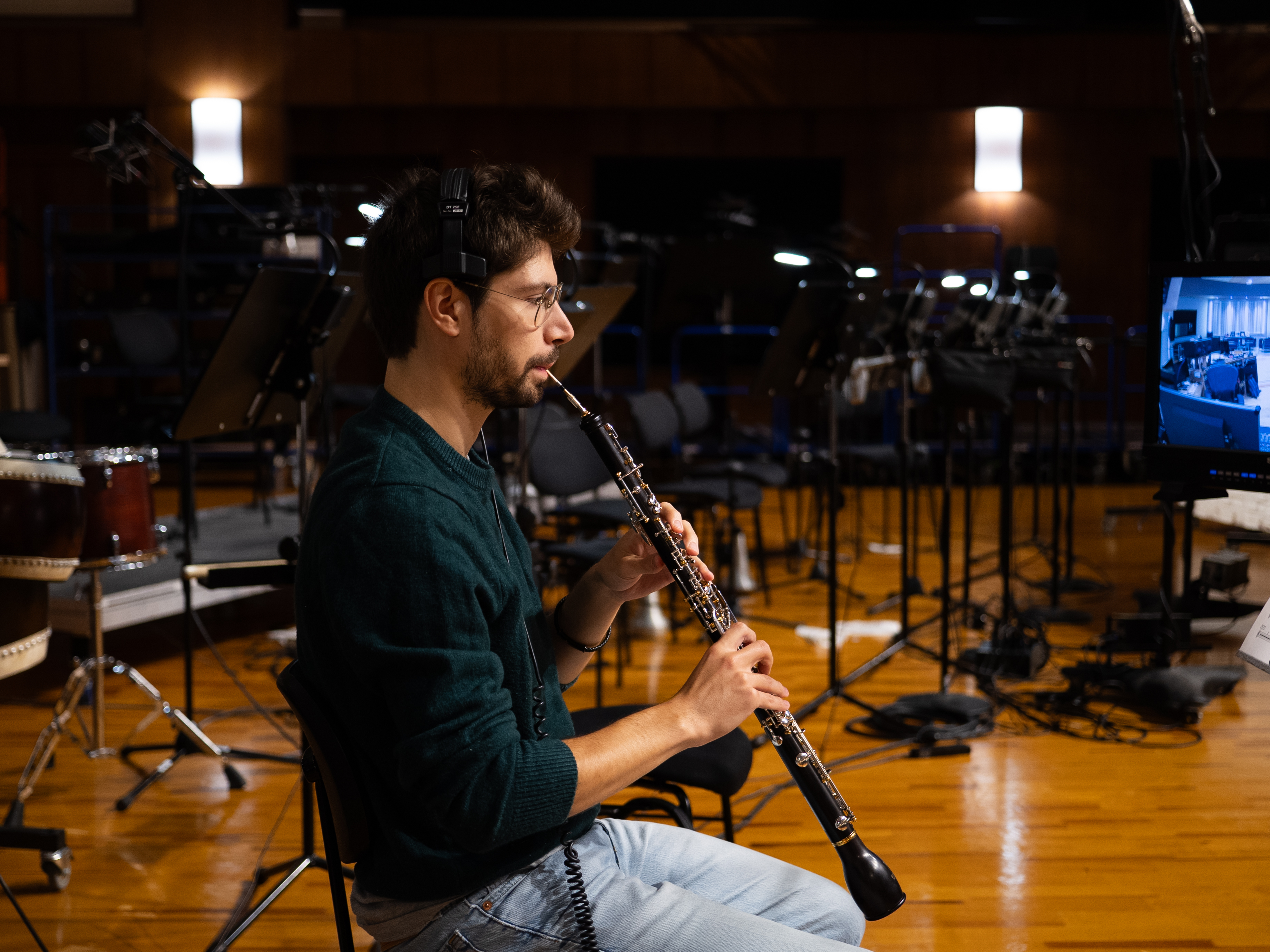 Musician playing an oboe in a recording studio, wearing headphones, surrounded by recording equipment for woodwind instruments.