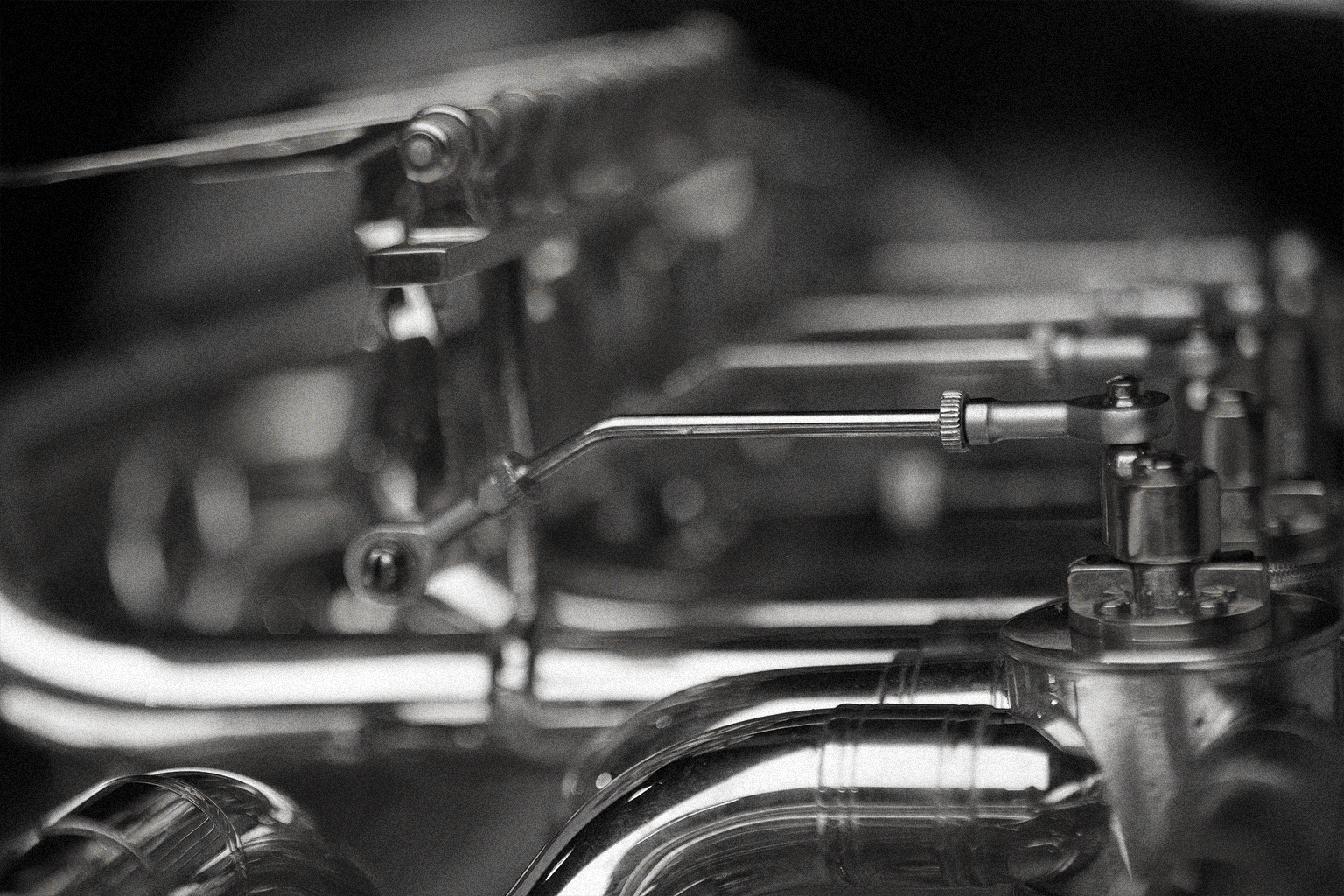 Close-up black and white photo of shiny brass instrument mechanisms, pipes, and levers, including detailed keywork and tubing.