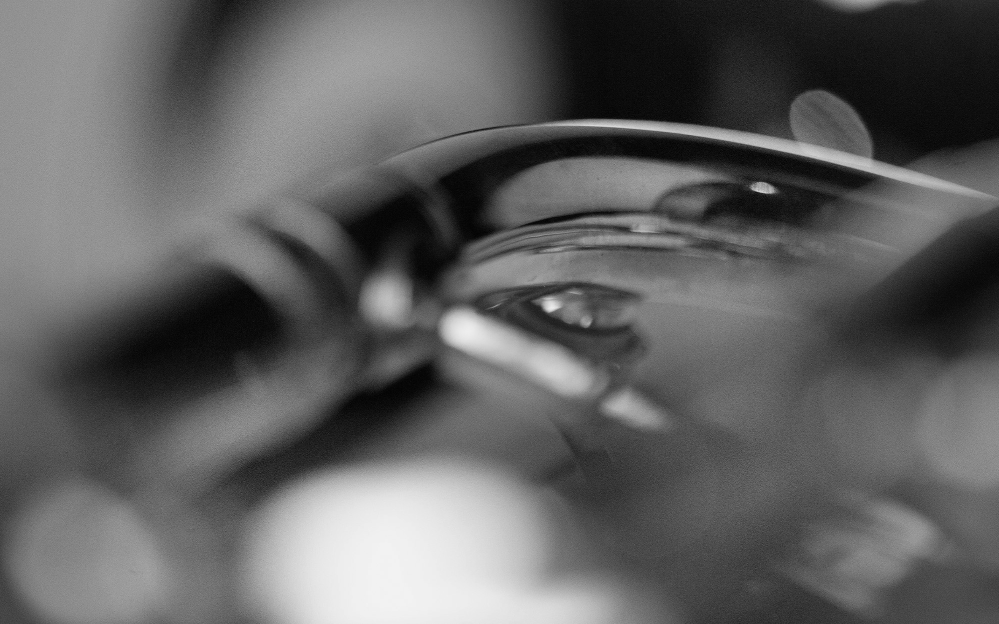 Abstract close-up in black and white, featuring a curved, reflective surface displaying blurred reflections of light and shapes, possibly depicting distorted views through water or glass, with a soft bokeh background.