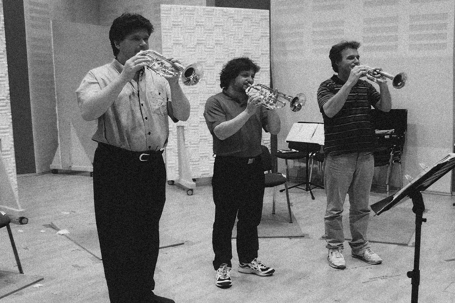 Three male musicians playing trumpets in a practice room, black and white photo.