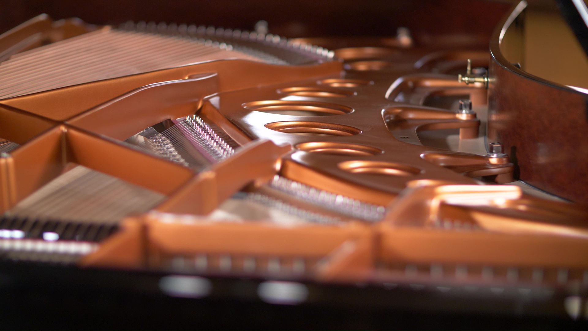 Interior view of a grand piano showing the golden harp, strings, and tuning pins.