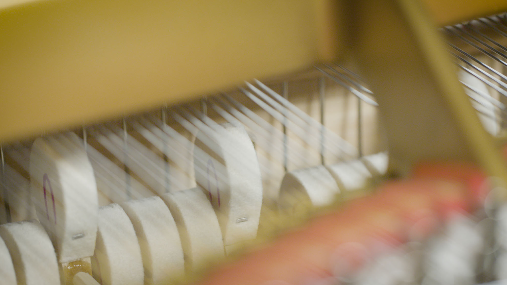 Close-up interior of an upright piano showing white hammer felts, thin strings, and golden soundboard with motion blur, illustrating the action mechanism.