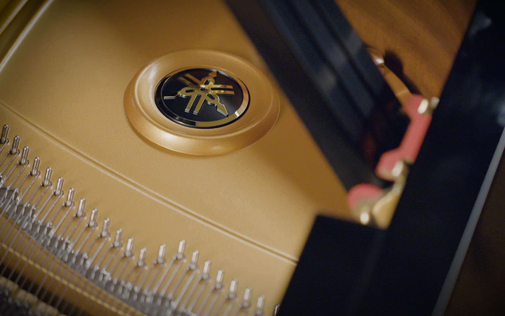 Close-up of a Yamaha grand piano soundboard with the gold Yamaha logo, strings, and tuning pins visible.