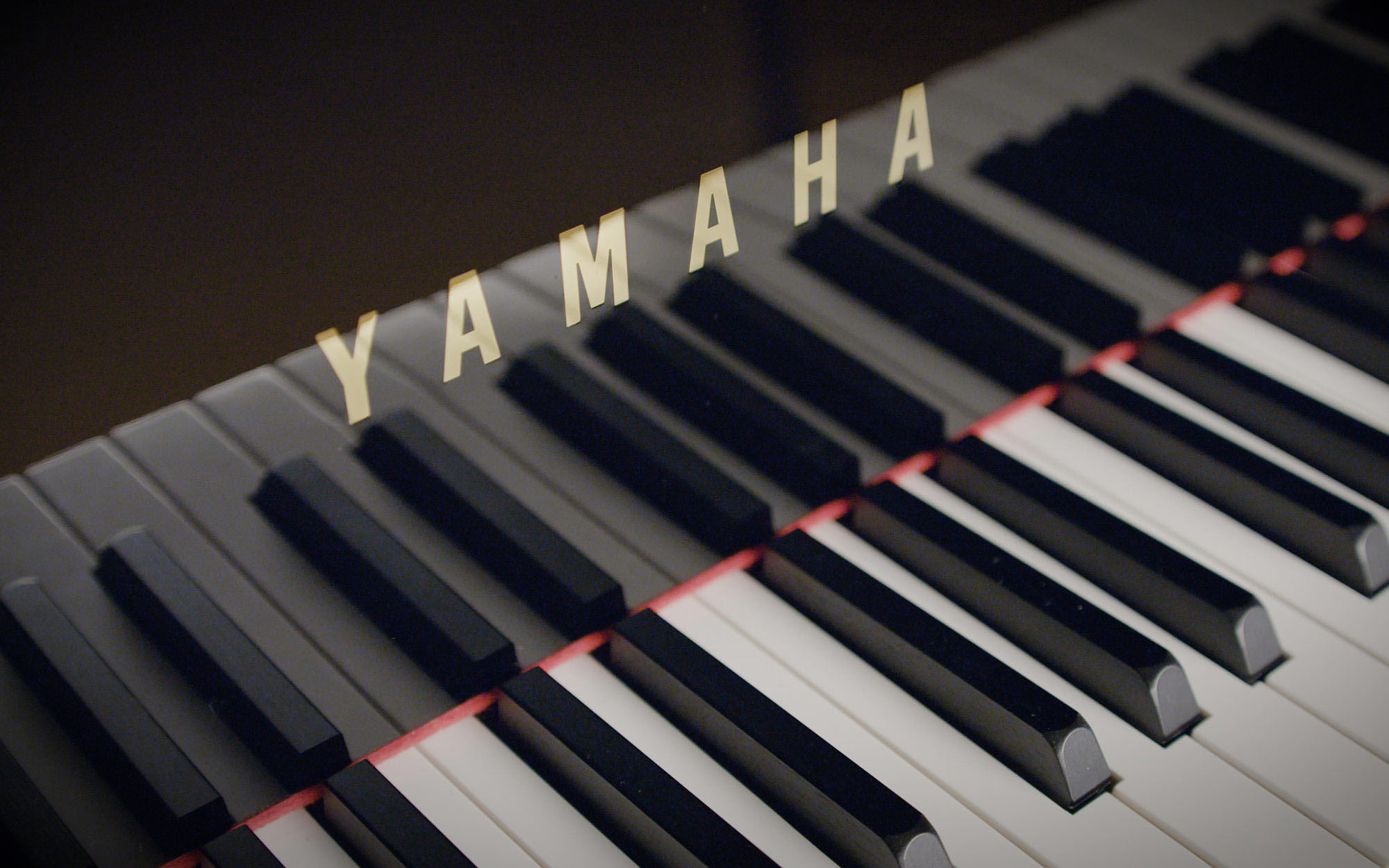 Close-up of a Yamaha piano keyboard, showing a full range of white and black keys with the golden Yamaha logo prominently displayed above them.