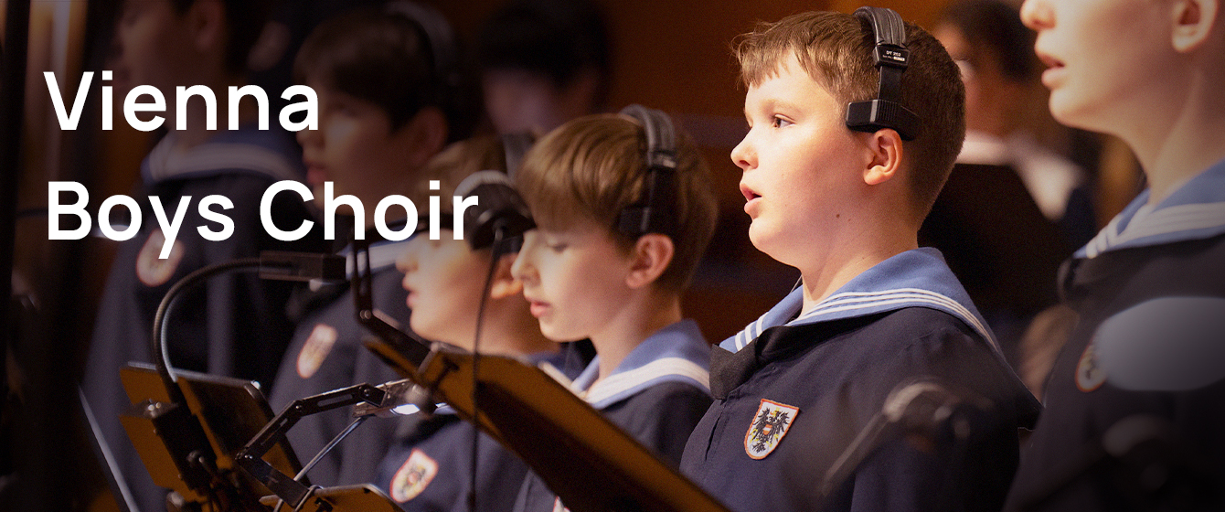 Vienna Boys Choir performing with headphones, wearing traditional navy uniforms with sailor collars and embroidered crests.