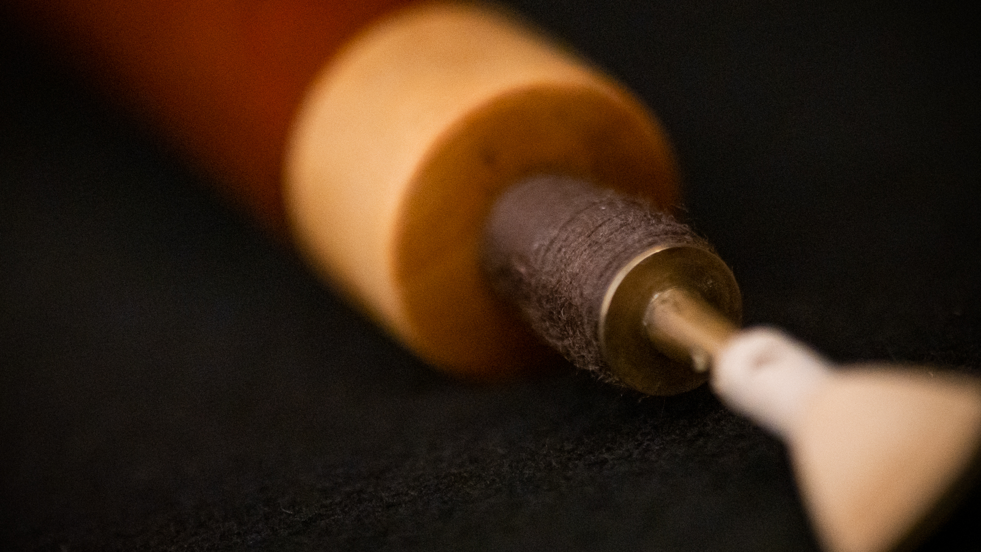 Detailed close-up of a bassoon bocal reed instrument part, showcasing its texture and assembly from a wooden or cork body, a dark wrapped threading, and a brass pipe leading to a light-colored reed.