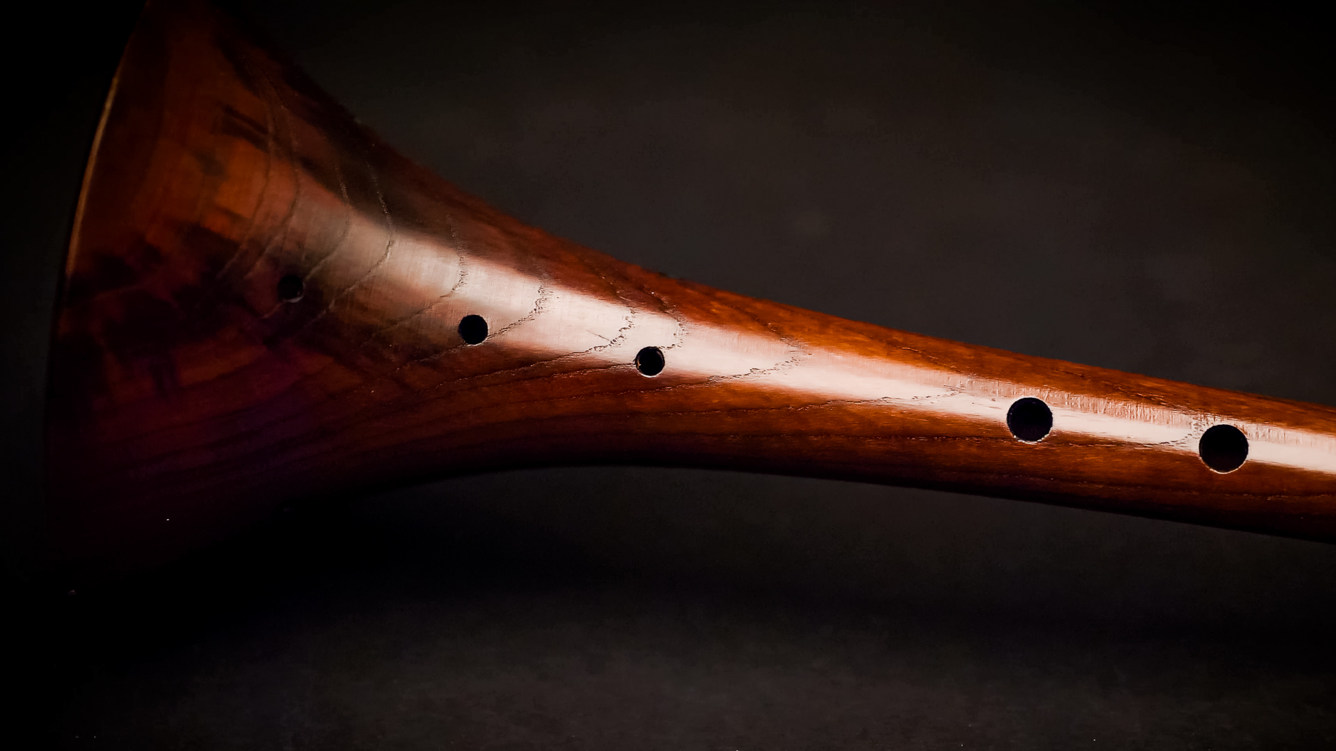 Close-up of a glossy, reddish-brown wooden wind instrument with several dark finger holes positioned against a dark background